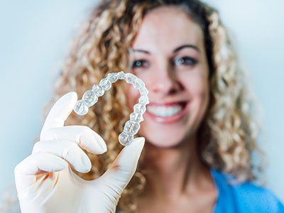 A woman is holding a transparent dental retainer in her hand, with a smile.