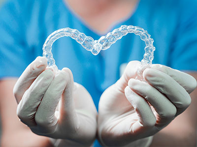 A dental professional holding a transparent model of a heart-shaped mouthguard, emphasizing oral health care.