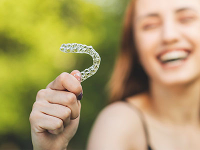 The image shows a person holding a clear plastic toothbrush with bristles, smiling at the camera.