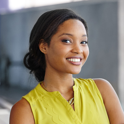 A smiling woman with dark hair, wearing a yellow top and standing against a neutral background.