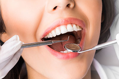 The image shows a woman in a dental setting, holding a toothbrush and engaging with a dental drill on her teeth.