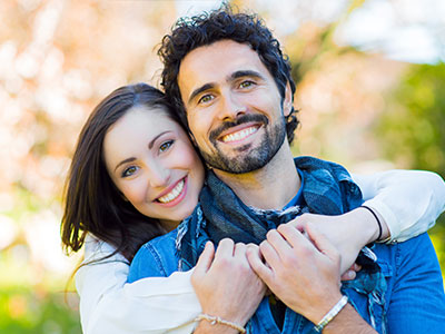 The image shows a man and a woman smiling at the camera, with the man wearing a dark shirt and the woman in a light-colored top.