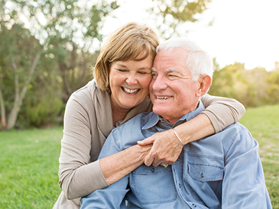 An elderly couple embracing each other outdoors.