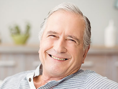 The image shows an elderly man with a smile, sitting in what appears to be a home setting.