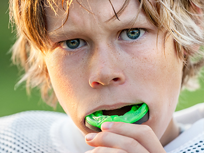 A young male athlete brushing his teeth with a green toothbrush.